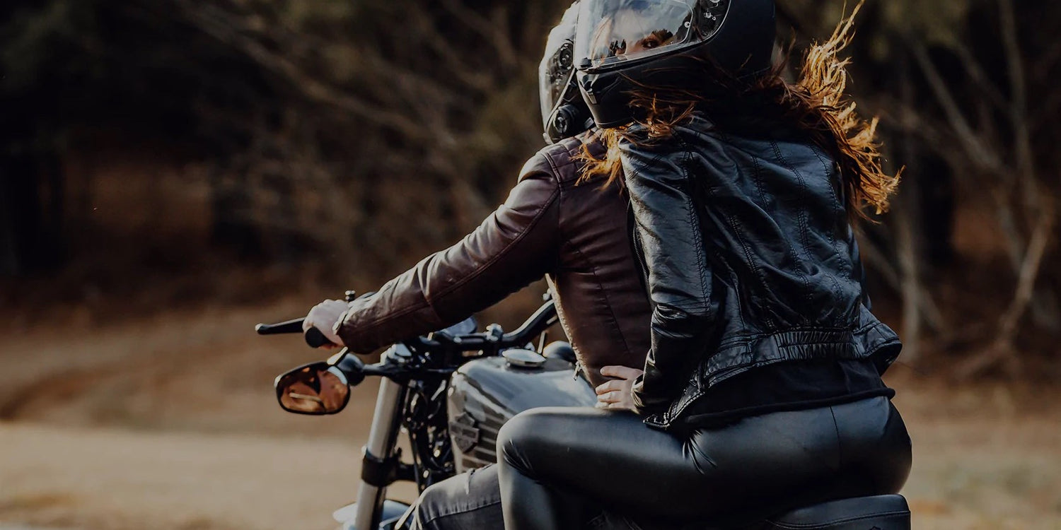 Young male and female couple riding in tandem on Harley Davidson sport motorcycle wearing black and brown leather riding jackets